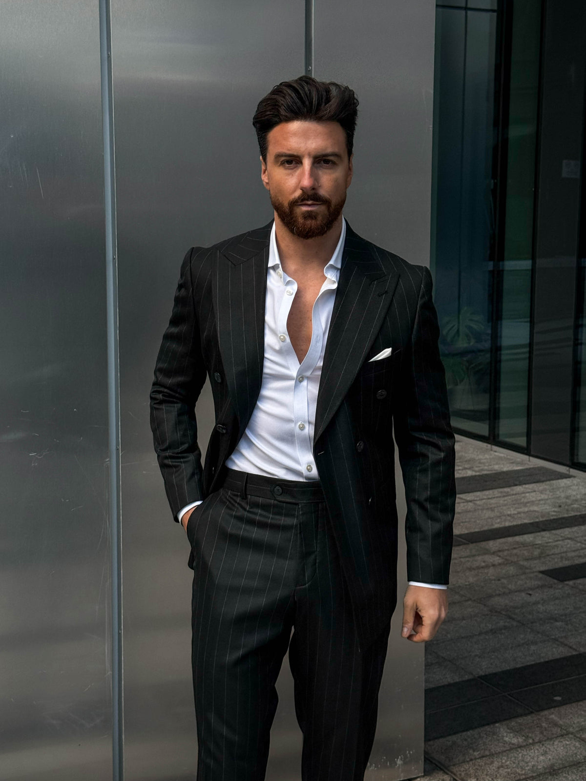 Man in a black suit standing against a modern building exterior